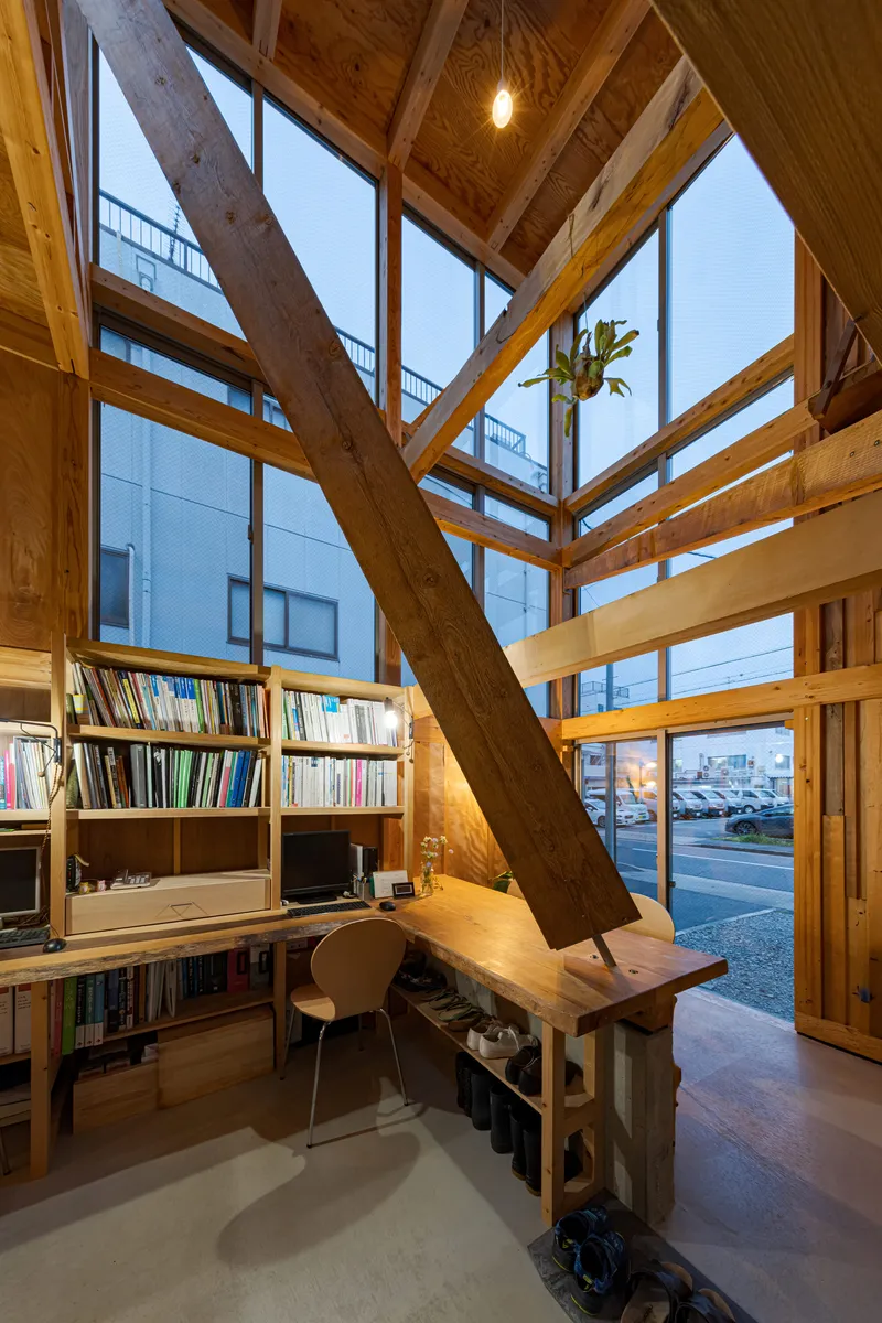 Work area with bookshelves beneath diagonal timber bracing and full-height glazing at dusk