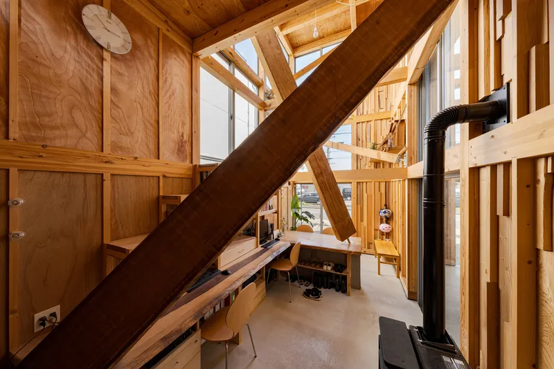 Interior space with diagonal timber bracing above a low desk and black metal stove