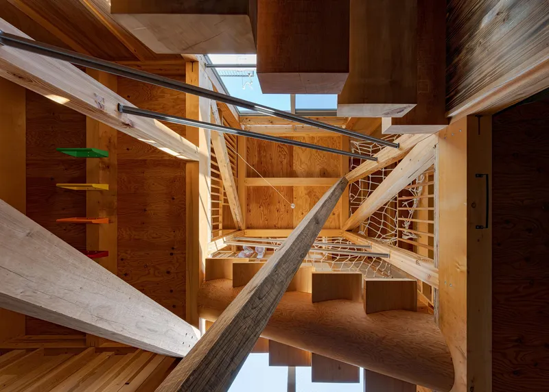 Looking up through the open timber stair structure with crisscrossing beams and skylights overhead