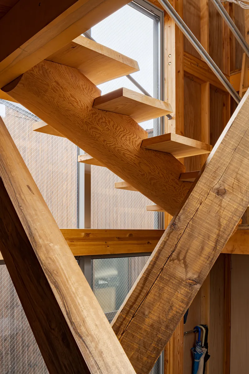Thick timber diagonal braces framing a zigzag stair with glass mesh safety panels in daylight