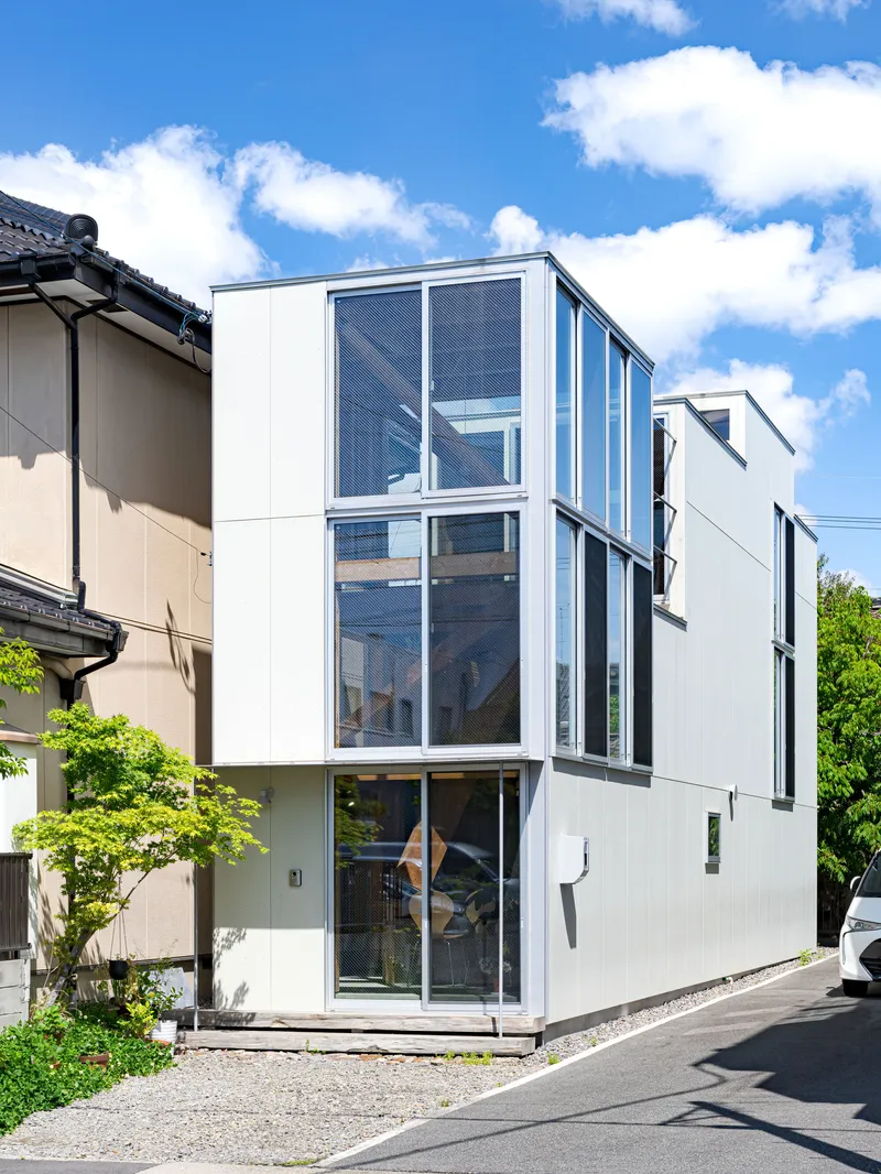 Three-story white facade with full-height glazing and metal screens under a blue sky