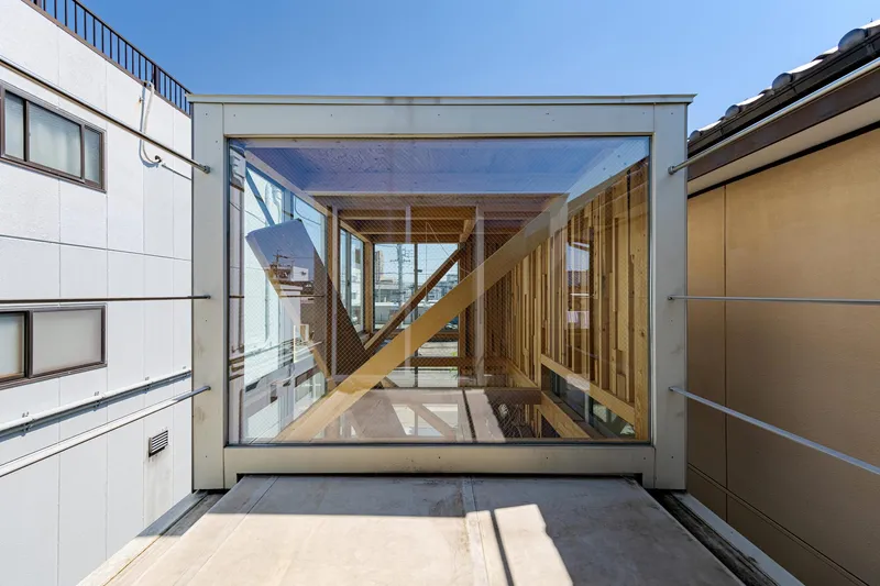 Glass-enclosed timber staircase framed by white walls in a rooftop courtyard under clear blue sky