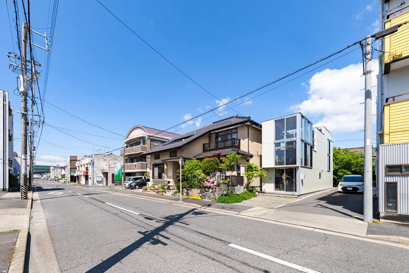 Street view showing a white box volume inserted between traditional houses under power lines and blue sky