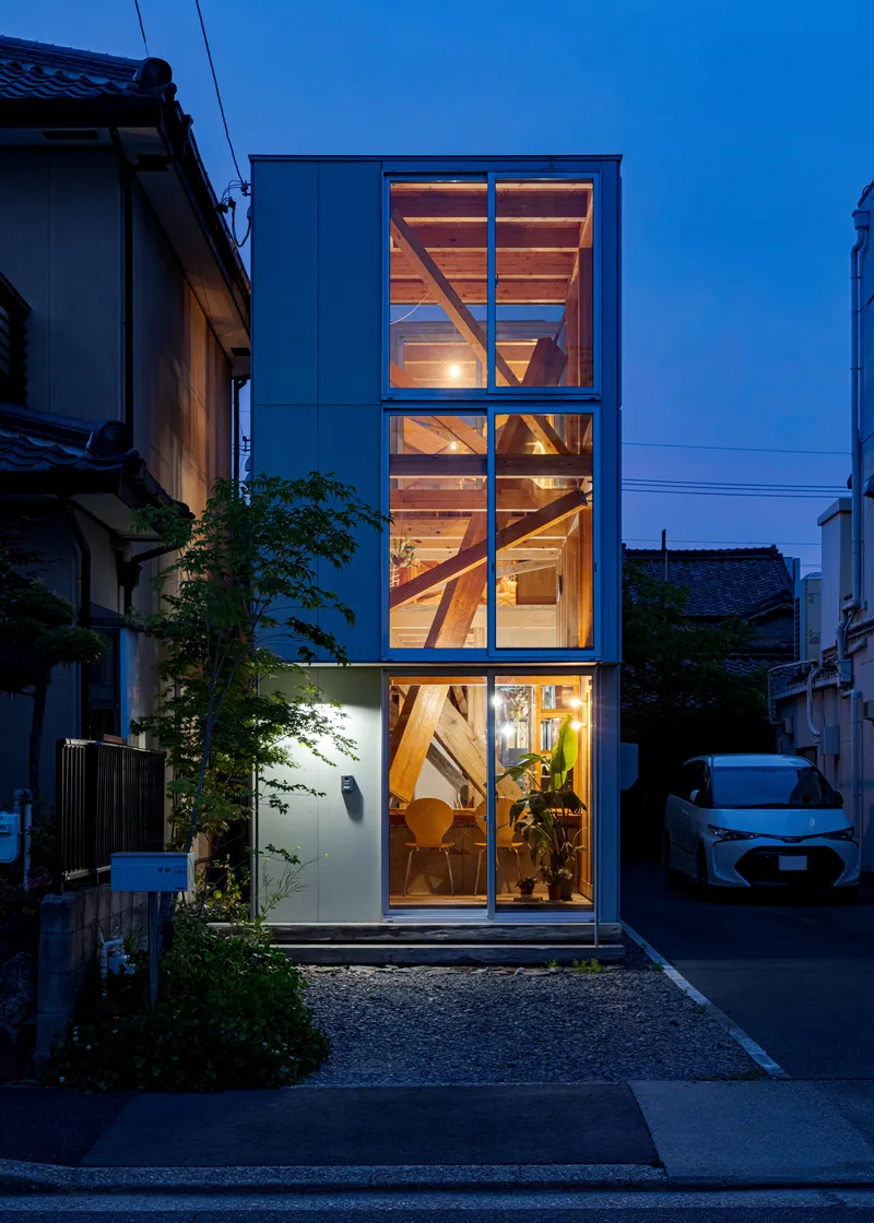 Street-facing facade with three stacked glazed bays revealing the timber staircase at twilight