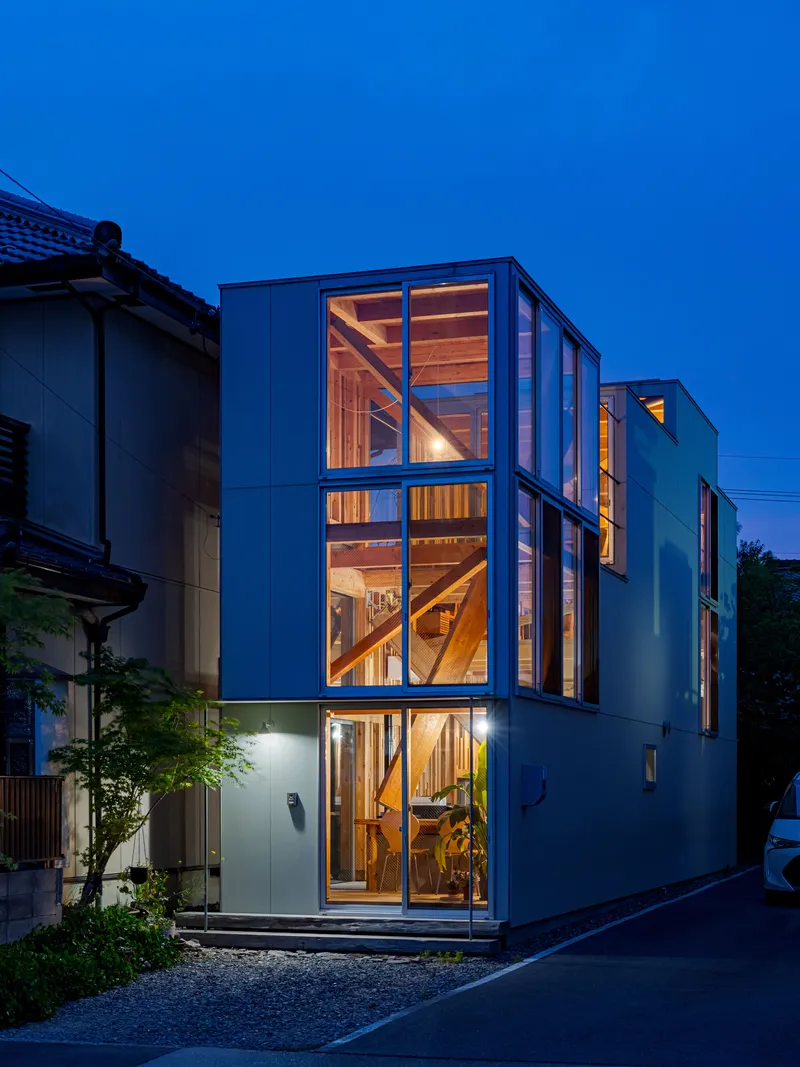 Facade showing the full-height glazing and diagonal timber stair structure at blue hour