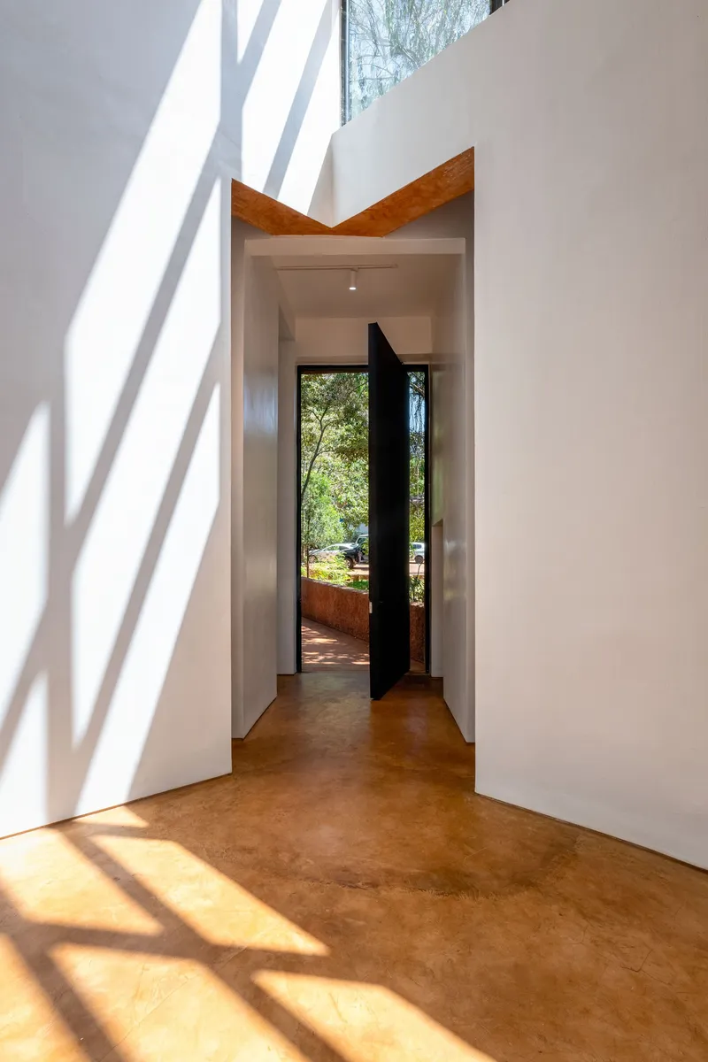 White interior corridor with timber door header and tree shadows falling across polished earth floor
