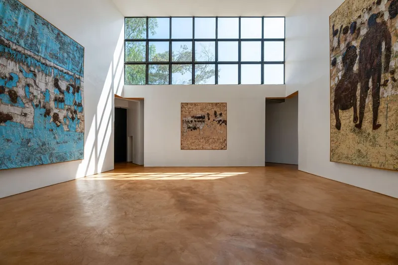 Double-height gallery space with gridded clerestory window and artworks on white walls in morning light