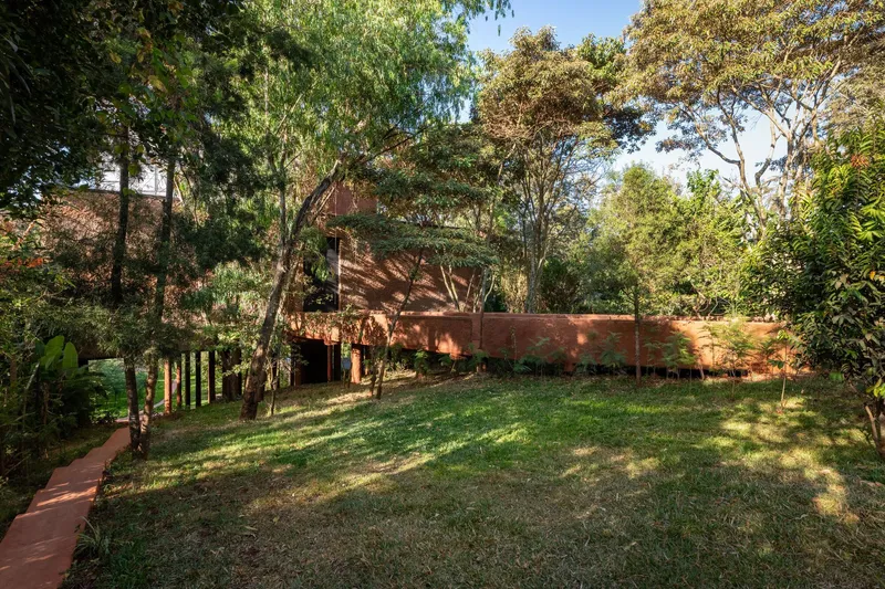 Garden view of red earth volumes connected by sloped roofs nestled among eucalyptus and tropical vegetation