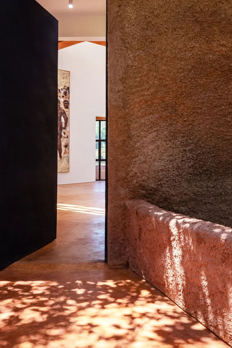 Entry threshold with rammed earth wall and bench catching dappled afternoon light on polished floor