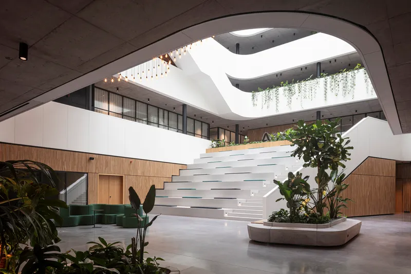 Multi-level atrium with curving white staircase, timber cladding and planters with tropical foliage below a skylight