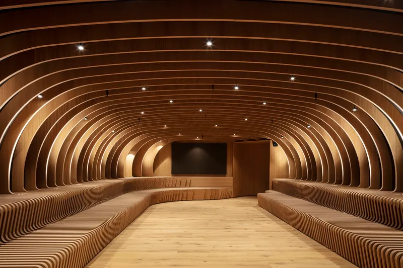 Arched timber ribs forming continuous walls and ceiling with integrated bench seating and recessed spotlights