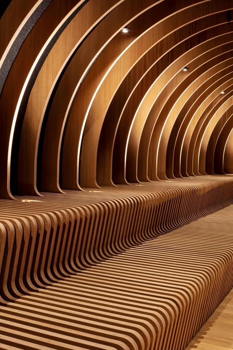 Close-up of laminated timber ribs curving to form both bench seating and wall surface under warm lighting