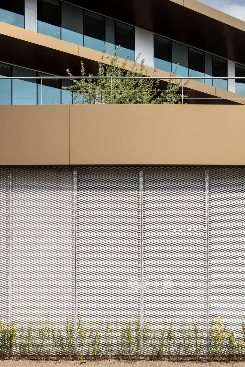 Expanded metal mesh screen below a tan parapet with planted trees visible above