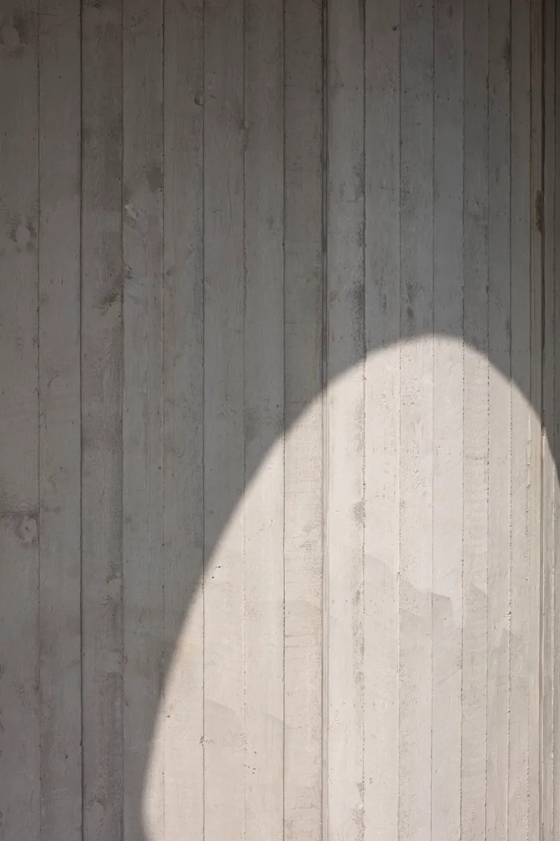 Board-formed concrete wall with an arched shadow cast by overhead structure