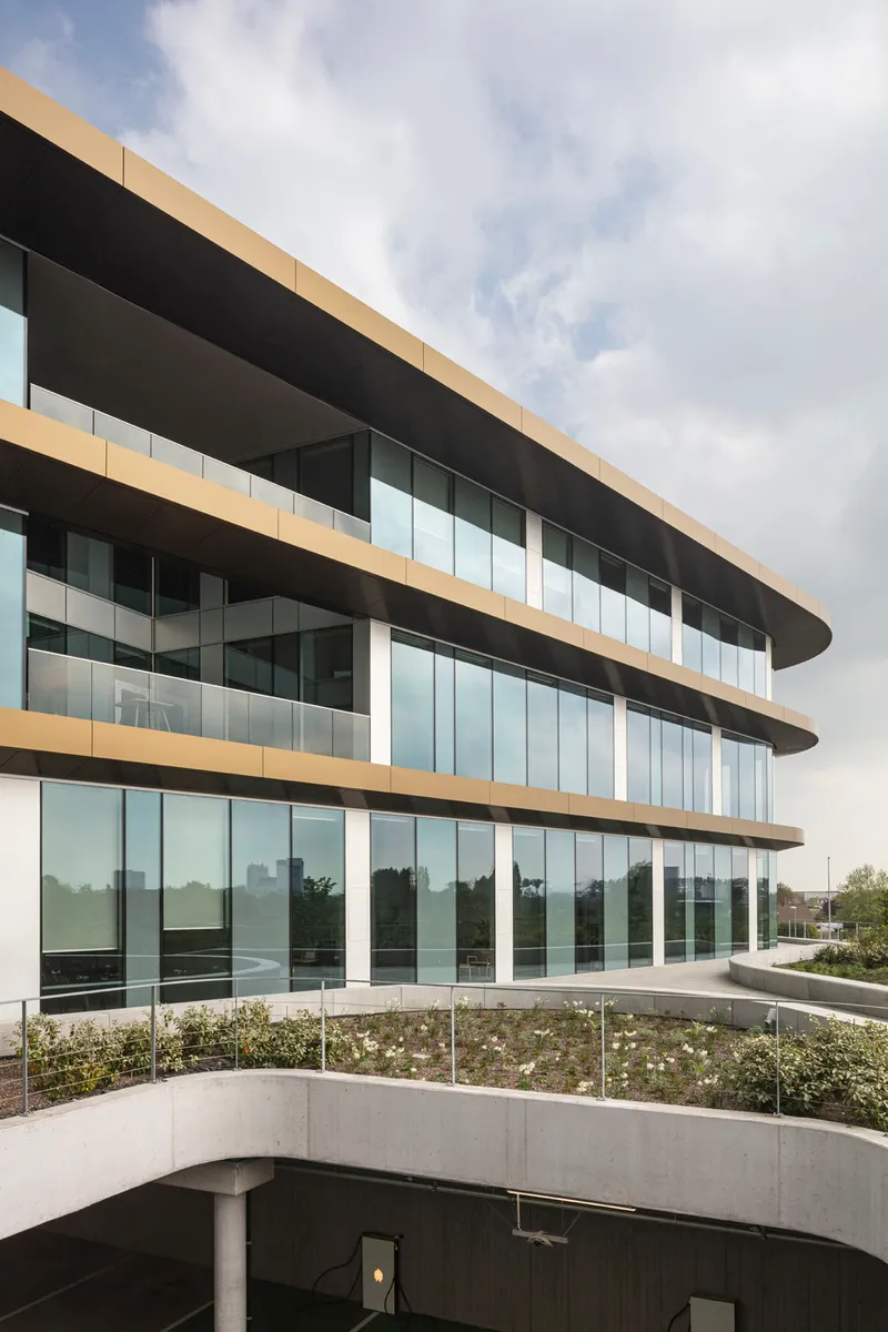 Three-story glass facade with horizontal metal banding above a curved concrete planter bed