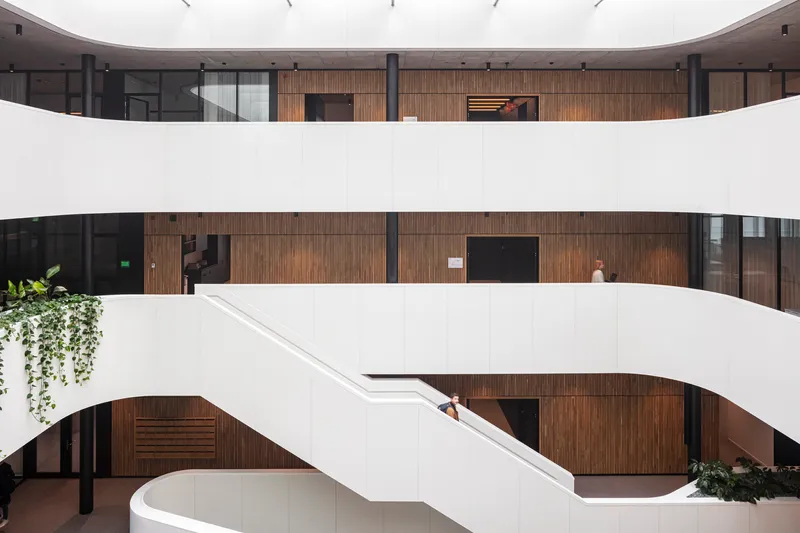 Curved white balconies overlooking timber-clad walls and a sculptural white staircase with trailing greenery