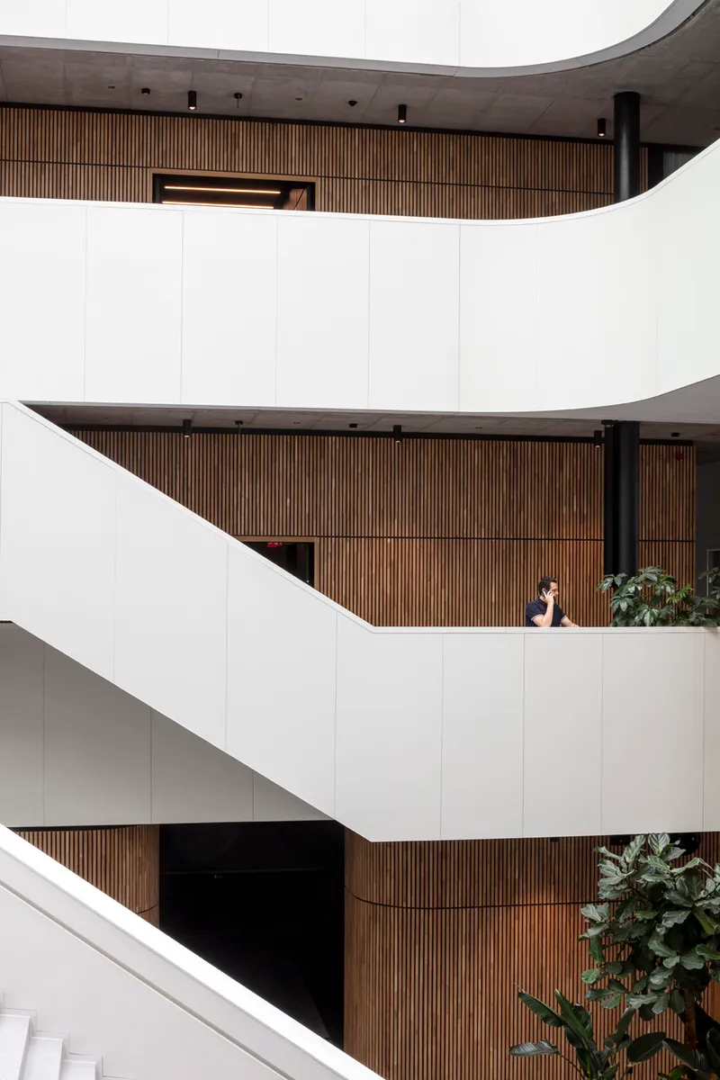 Stacked white balconies with timber slat cladding and a person seated at mid-level next to potted plants