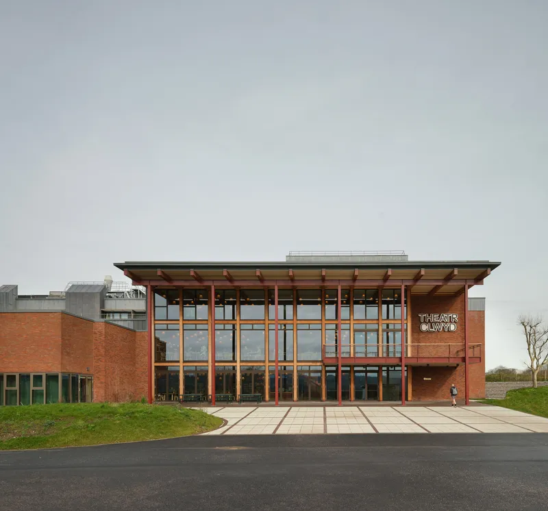 Entrance facade with timber columns and cantilevered roof over glazed curtain wall in overcast light
