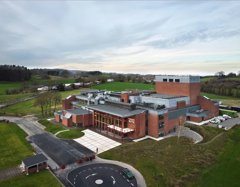 Aerial view of the red brick complex with flat roofs and mechanical equipment in surrounding farmland