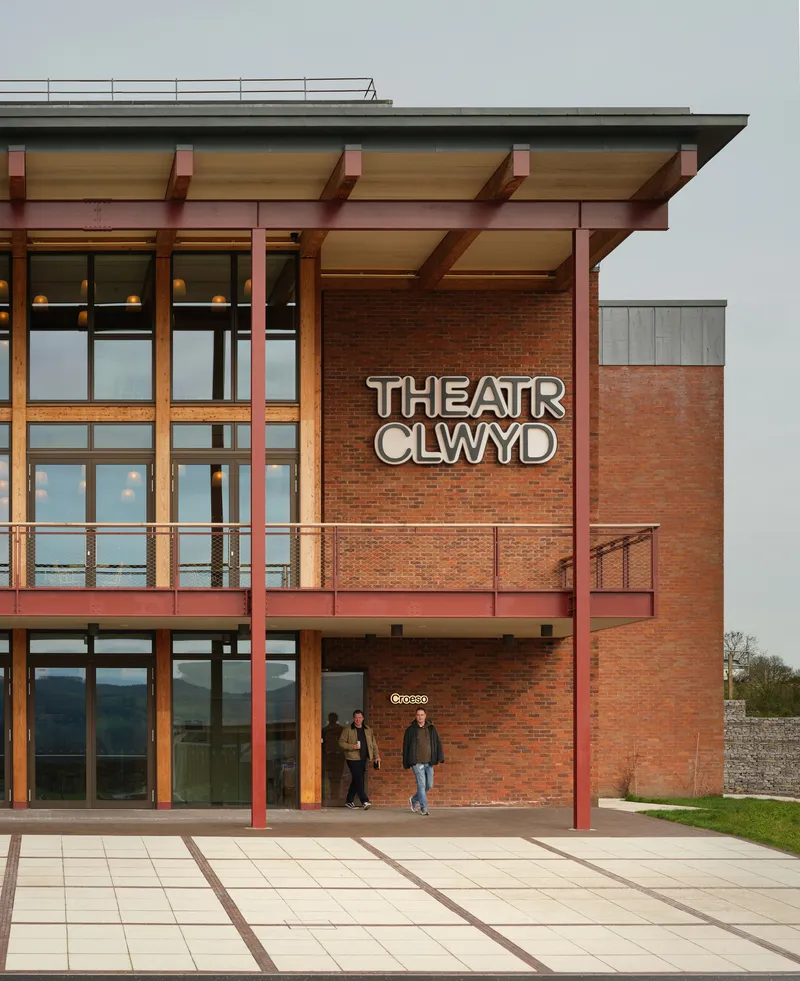 Two-story brick facade with steel columns, cantilevered canopy and visitors walking below signage