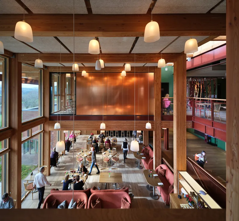 Double-height dining hall with exposed timber beams, white pendant lights, and copper wall panels