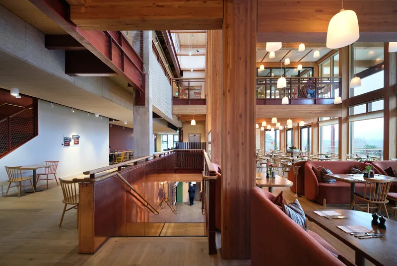 Multi-level interior with timber columns, red steel railings, and mountain views through glazed walls