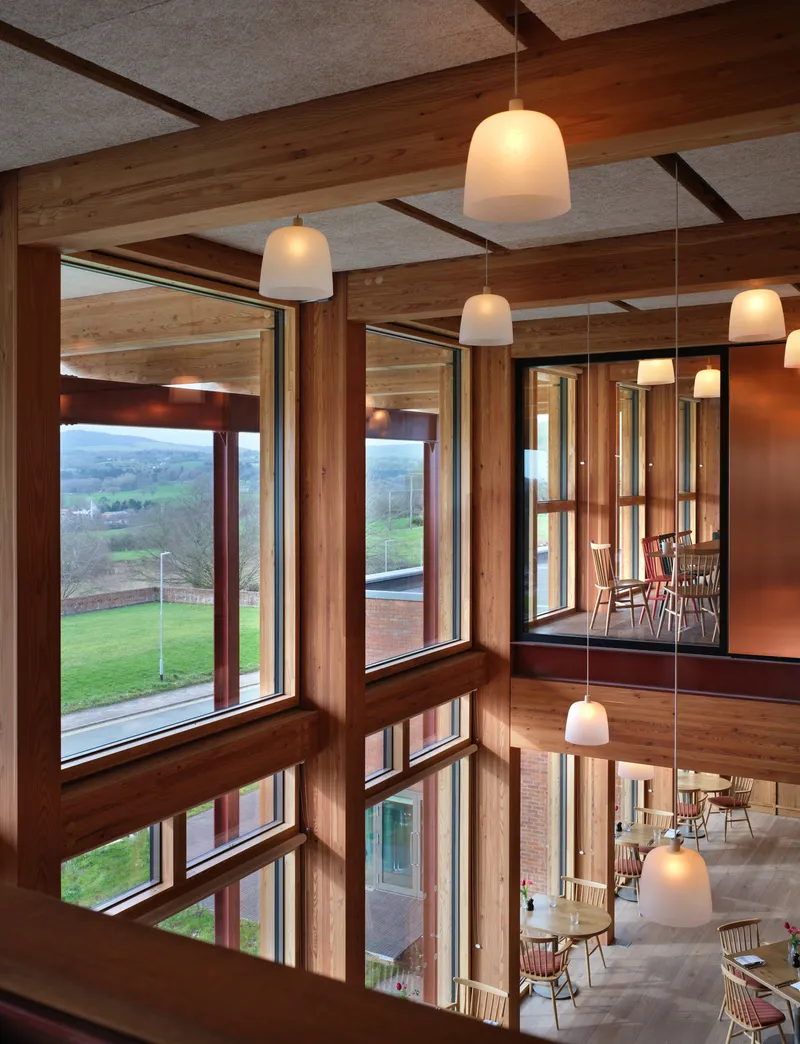 Corner windows framing countryside view with timber mullions and pendant lights reflected in glass