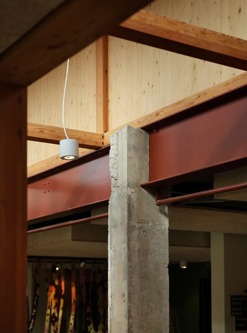 Junction detail of concrete column, red steel beam, and timber roof structure with pendant light