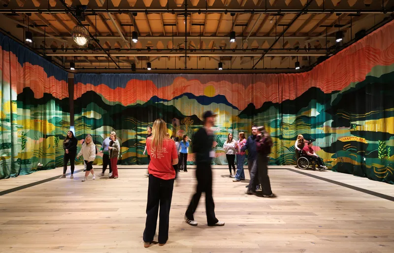 Interior hall with colorful landscape mural on glass partition and people gathered in groups