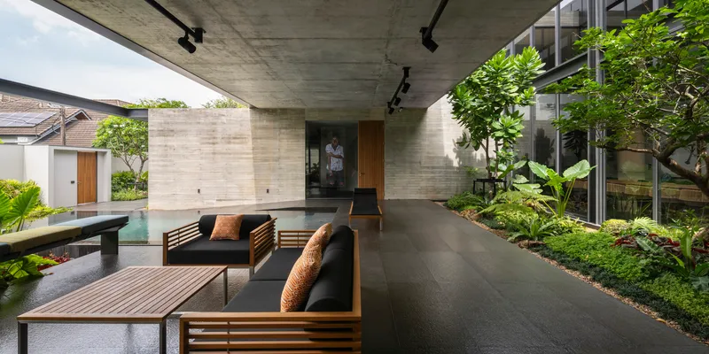 Covered outdoor lounge beneath exposed concrete soffit with timber furniture adjacent to lap pool and planted beds