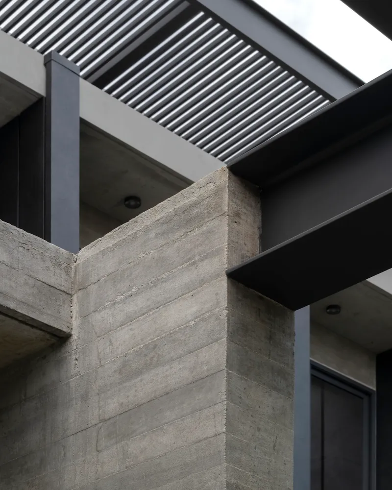 Board-formed concrete corner column meeting dark metal beams and overhead louver screen