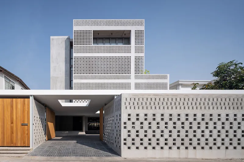 Street view of the perforated white facade and covered entry drive under a clear blue sky