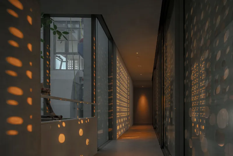 Interior corridor at dusk with perforated screens casting oval light patterns on walls and floor