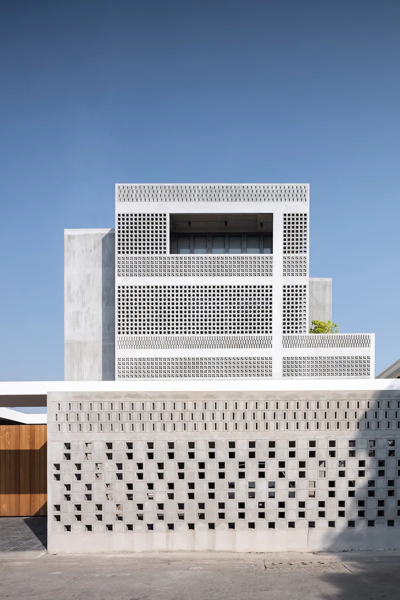 Layered white concrete screens with square perforations and recessed glazing on the upper facade