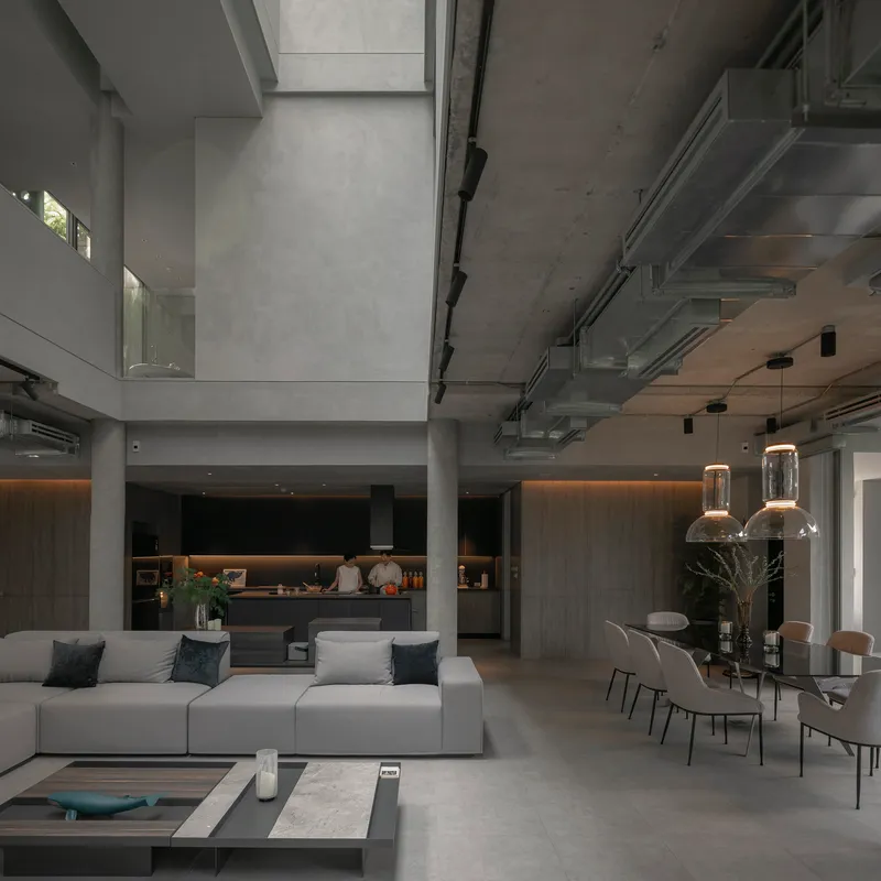 Open-plan living area with exposed concrete ceiling, pendant lights, and a kitchen beyond