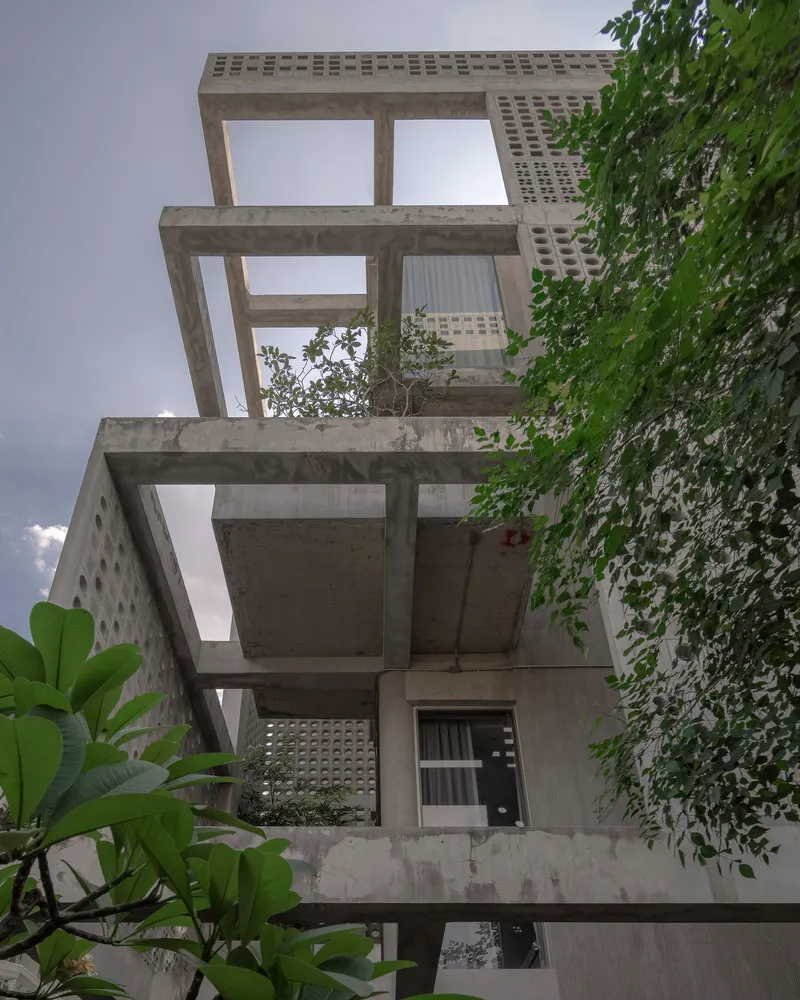 Stacked concrete terraces with perforated screens and planted balconies framed by banana leaves