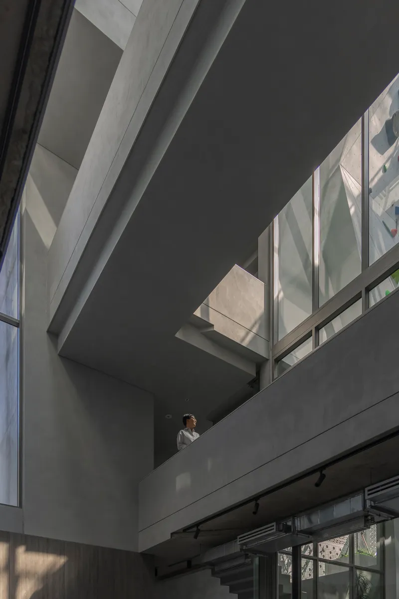 Interior atrium view showing overlapping concrete balconies with a single person standing in dappled sunlight