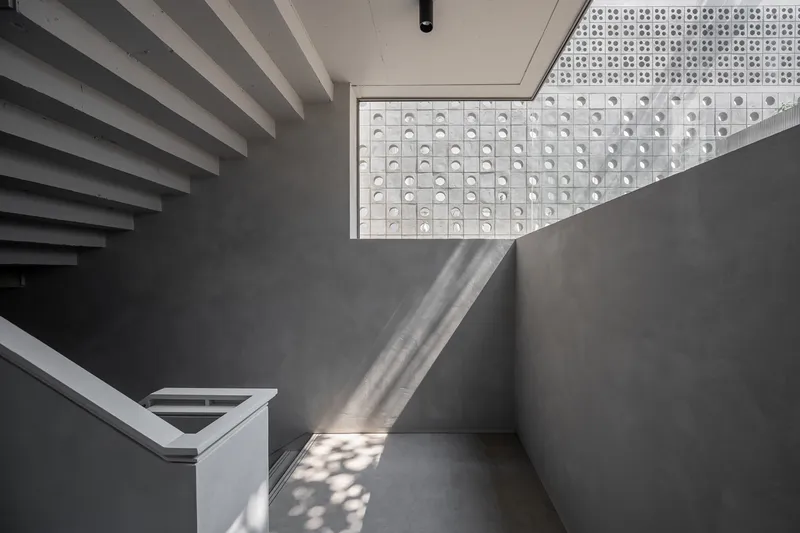 Stairwell landing with horizontal louvered wall and perforated screen visible through skylight above