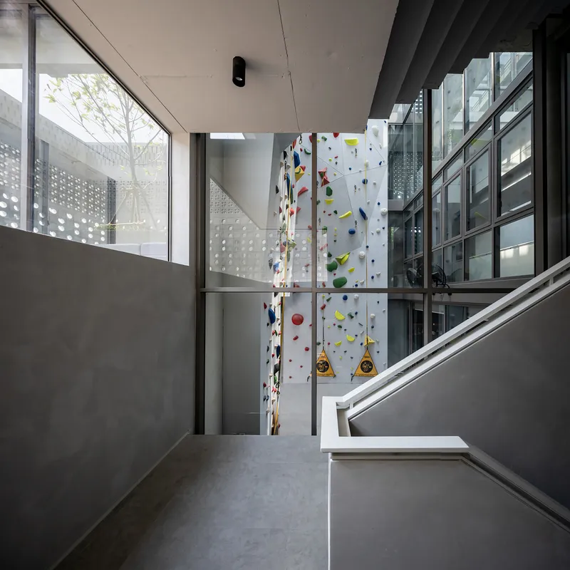 Staircase landing overlooking vertical climbing wall and glazed courtyard with perforated facade in background