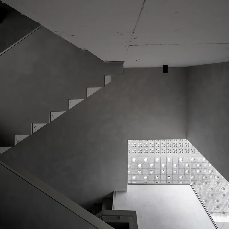 Looking up at cantilevered concrete stairs against a perforated glass block wall filtering natural light