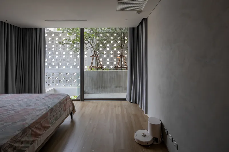 Bedroom with timber flooring opening onto a planted balcony framed by grey curtains and perforated concrete screen