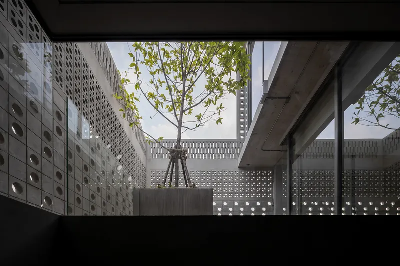 Rooftop courtyard with a single tree in a planter surrounded by perforated concrete block walls under open sky