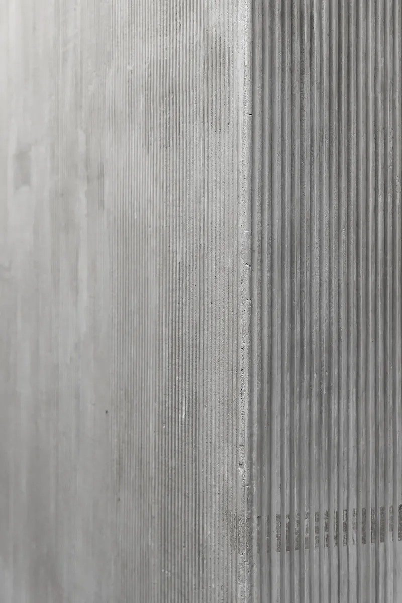 Close-up of cast concrete wall surface showing vertical ribbed formwork texture and seam joint