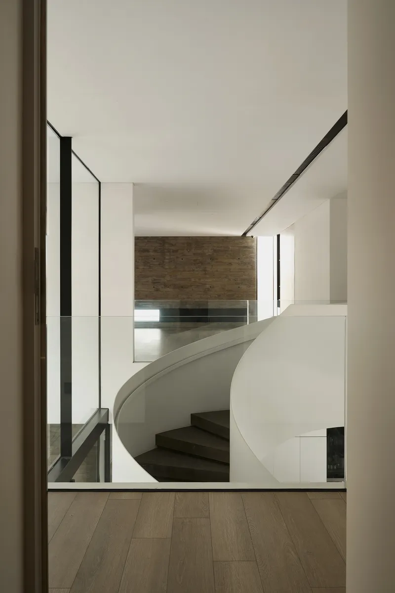 View through a doorway to the curved white staircase descending toward a timber-clad wall