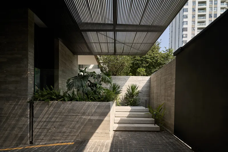 Exterior courtyard with timber slatted pergola casting shadows over planted beds and concrete steps