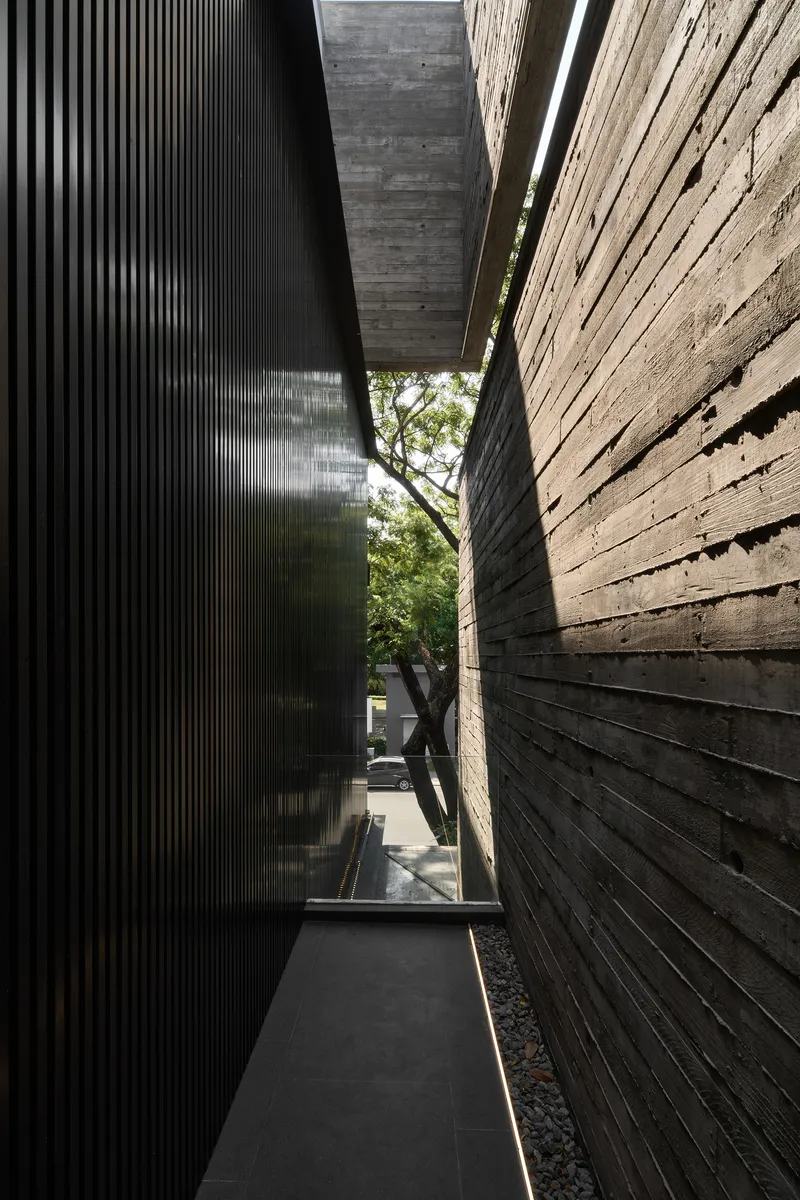 Narrow passage between board-formed concrete walls with a glimpsed tree beyond the opening