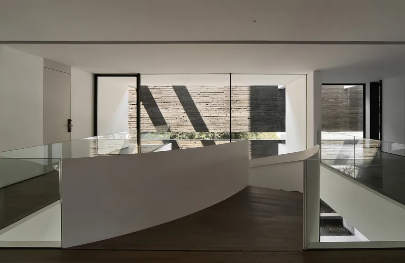 Upper landing with curved glass balustrade overlooking a courtyard through large windows