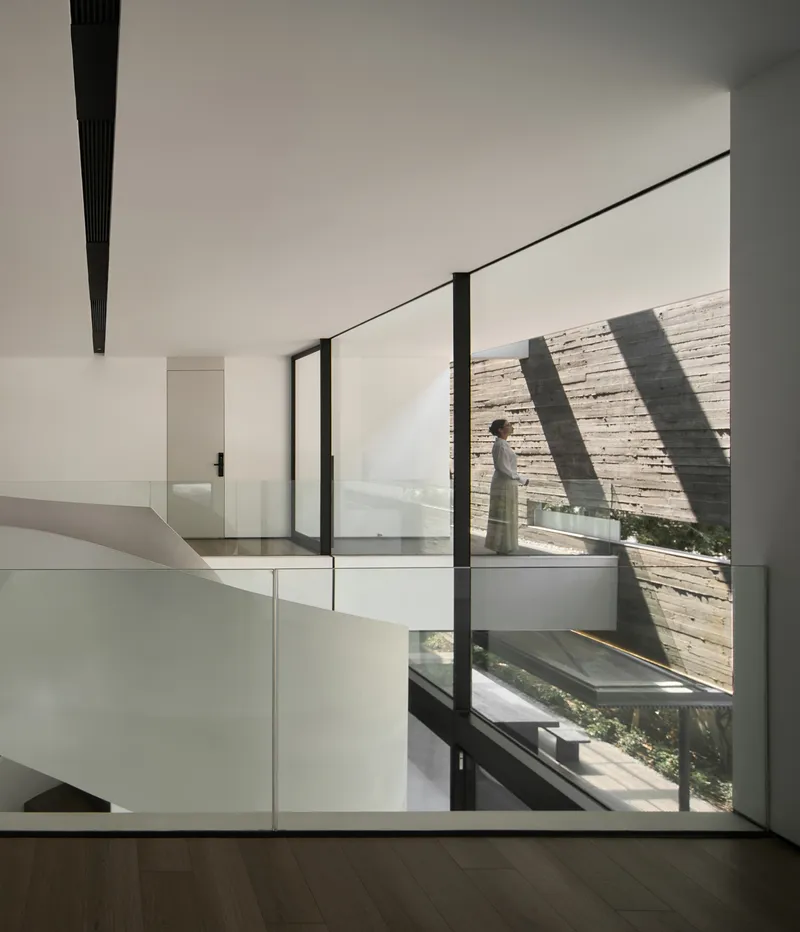 Interior hall with a figure walking past full-height glazing onto a courtyard terrace