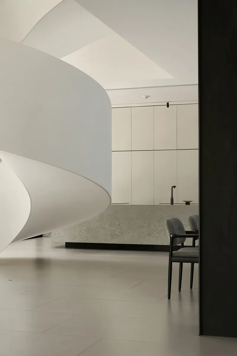 White curved staircase descending beside a terrazzo island and pale paneled cabinetry