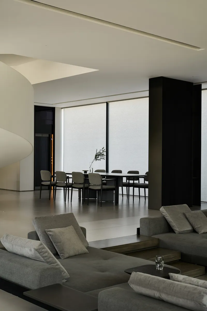 Living room with grey sofas looking through black columns toward a dining table by a window